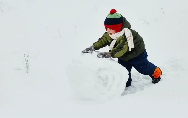 Young child in a coloured beanie making a huge snowball